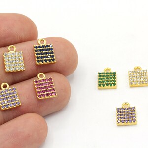 May include: Gold-toned square charms with colorful gemstones. The charms feature a rectangular shape with a loop at the top for attaching to jewelry. Gemstones are arranged in rows, with colors including green, white, blue, purple, and pink.