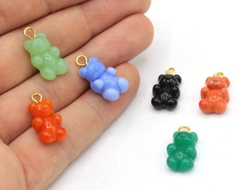 Könnte beinhalten: Eine Sammlung bunter Gummibärchen-Anhänger in Grün, Blau, Schwarz, Orange und Rot. Jeder Anhänger hat eine goldfarbene Schlaufe zum Befestigen an Schmuck oder anderen Bastelarbeiten. Die Anhänger sind klein und haben ein glänzendes Finish.