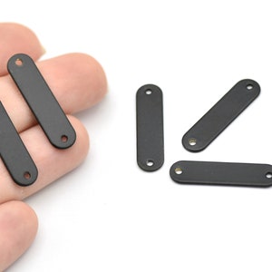 May include: A collection of matte black metal bar connectors, each with two holes, are shown against a white backdrop. These small, rectangular components are suitable for jewellery making or craft projects.