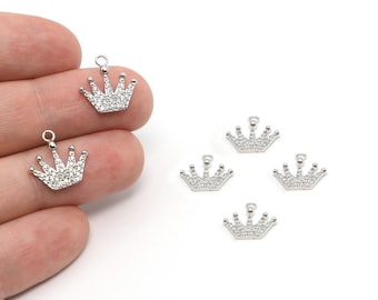 May include: Several small, silver-colored crown charms with clear, sparkling accents are displayed against a white background. Each charm has a loop at the top for attaching to jewelry. The charms are arranged in a scattered pattern.