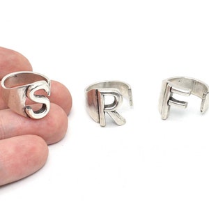 May include: Three silver-colored rings, each featuring a different letter: S, R, and F. The rings have a simple, open design, with the letters prominently displayed. The rings are likely adjustable, with a gap in the band.