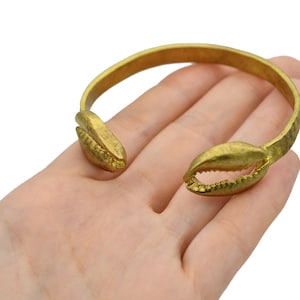 May include: A gold-colored cuff bracelet with a claw design. The bracelet features two claw-shaped ends with detailed textures and a smooth, rounded band. The open design allows for easy wear. The bracelet is shown on a white background.