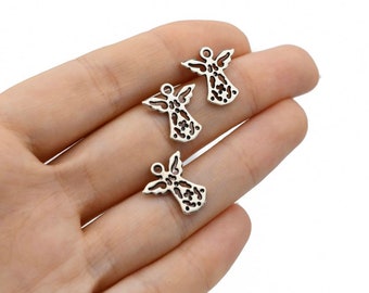 Puede incluir: Se muestran tres pequeños dijes plateados con forma de ángel y diseños calados. Cada dije tiene alas extendidas y un lazo en la parte superior para sujetarlo a la joyería. Los dijes se sostienen en una mano sobre un fondo blanco.