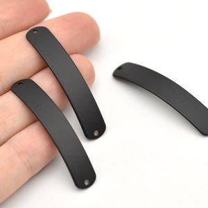 May include: A collection of black, curved metal jewelry components. Each piece has a smooth, matte finish and a small hole at each end, suggesting they are designed for stringing or connecting. The pieces are displayed against a white background.