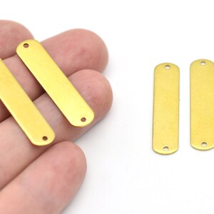 May include: Four rectangular brass metal jewelry findings with rounded ends and two holes for attaching to other components. The findings are a warm gold color and are shown against a white background.