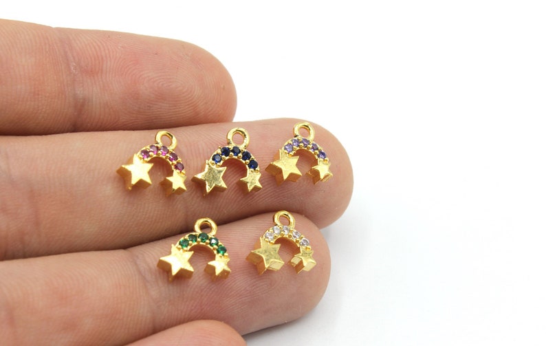 May include: Gold-coloured star charms with a rainbow arch of colourful gemstones. Each charm features two stars and a curved row of gems in various colours, including red, blue, purple, green, and clear.