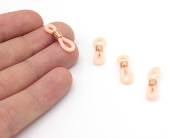 May include: Several peach-colored eyeglass retainers with gold-colored metal coils. The retainers are in a loop shape, designed to attach to the arms of eyeglasses. The background is white.