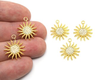 Può includere: Ciondoli a forma di sole color oro con un centro scintillante simile a cristalli e raggi radianti. Ogni ciondolo ha un piccolo anello nella parte superiore per il fissaggio ai gioielli. I ciondoli sono esposti su sfondo bianco.