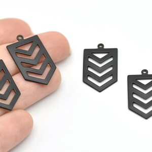 Könnte beinhalten: Schwarze Metallanhänger in Pfeilform mit einem ausgeschnittenen Chevron-Design. Jeder Anhänger hat oben eine kleine Schlaufe zum Befestigen an Schmuck. Die Anhänger werden vor weißem Hintergrund gezeigt.