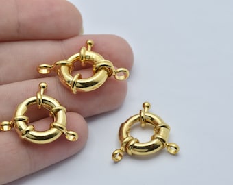 Könnte beinhalten: Drei goldfarbene, runde Schmuckverschlüsse. Jeder Verschluss hat eine Ringform mit einem Mittelsteg und einem kleinen, dekorativen Pfosten. Die Verschlüsse sind mit kleinen Schlaufen zum Befestigen an Schmuckstücken versehen.