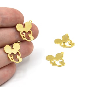 Puede incluir: Encantos de metal dorado con forma de cabeza de rat&oacute;n con remolinos decorativos. Los encantos tienen un peque&ntilde;o lazo en la parte superior para sujetarlos a joyas u otras manualidades. Varios encantos son visibles sobre un fondo blanco.