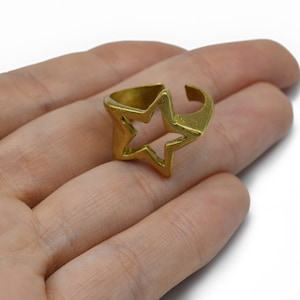 Op de afbeelding: Een goudkleurige ring in de vorm van een ster. De ring heeft een uitgesneden sterontwerp en een verstelbare band. De ring is gemaakt van een glanzend, metalen materiaal. De ring wordt op de hand van een persoon getoond.
