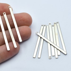 May include: A collection of silver-colored, rectangular metal bar charms with a small hole at one end. These jewelry-making components are displayed against a white background. The charms are ideal for creating necklaces, bracelets, and earrings.