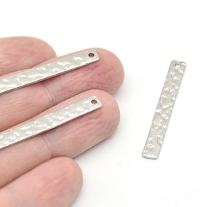 May include: Three silver-coloured, rectangular metal jewellery components with a hammered texture. Each component has a small hole at one end. The components are displayed against a white background.