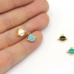 May include: Small, gold-colored planet charms with enamel details. The charms feature a planet design with a gold band and are available in white, light blue, black, and teal. These charms are ideal for jewelry making.