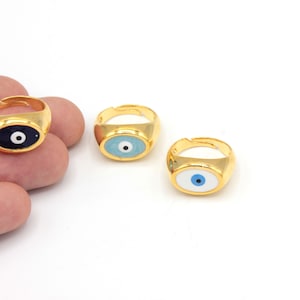 May include: Gold-toned adjustable rings with oval-shaped eye designs. The eyes are in blue, light blue, and navy blue with white and black details. The rings are on a white background.