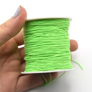 May include: A spool of bright neon green elastic cord. The cord is tightly wound around a white plastic spool. The image is a close-up shot, highlighting the texture and color of the cord. The cord is a vibrant, eye-catching green.