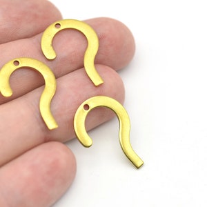 Op de afbeelding: Drie goudkleurige metalen bedels in de vorm van een vraagteken. Elke bedel heeft een klein gaatje aan de bovenkant om te rijgen. De bedels liggen op een witte achtergrond.