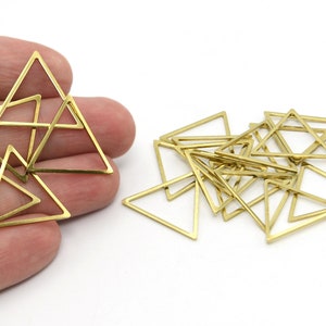 May include: A collection of small, open-frame brass triangles. Some triangles are grouped together, while others are scattered. The triangles are a warm gold color and appear to be jewelry findings or craft supplies.