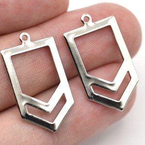 May include: Two silver-colored metal pendant charms. Each charm has a rectangular shape with a geometric cutout design and a small loop at the top for attaching to a chain or other jewelry component.
