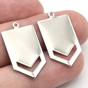 May include: Two silver-colored metal pendant charms. Each charm is rectangular with a cut-out chevron design at the bottom and a small loop at the top for attaching to a chain or other jewelry component. These are ideal for DIY jewelry making.