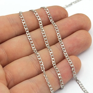 May include: A silver curb chain necklace is displayed in a person's hand. The chain has a repeating pattern of interlocking links. The background is a plain white surface.