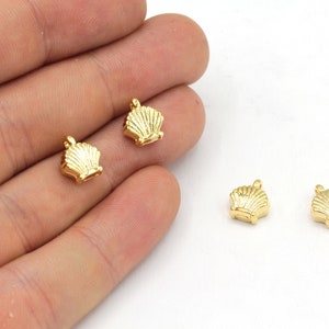 Peut inclure: Petits charms dorés en forme de coquillage. Ces pendentifs miniatures présentent un motif de coquillage détaillé avec une boucle en haut pour les attacher à des bijoux. Les breloques sont présentées sur fond blanc.
