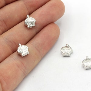 May include: Four small, silver-colored seashell charms. Each charm has a detailed shell design with a loop at the top for attaching to jewelry or other crafts. The charms are shown against a white background.