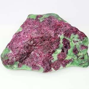 Pode incluir: Um espécime mineral bruto com uma forma rugosa e irregular, apresentando um contraste vibrante entre aglomerados cristalinos de cor magenta profunda e uma matriz lisa de cor verde-clara. A textura da superfície é variada, exibindo formações dentadas e cintilantes semelhantes a rubis e secções sólidas e opacas de zoisite verde.