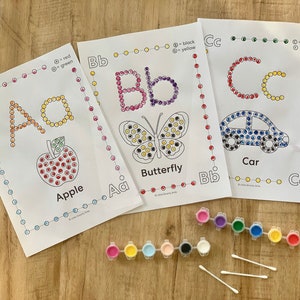 Pu&ograve; includere: Tre fogli di attivit&agrave; educative con le lettere Aa, Bb e Cc, caratterizzati da disegni a puntini di una mela, una farfalla e un'auto. Ogni foglio include chiavi di colore, due strisce di piccoli vasetti di vernice e tre bastoncini cotonati.