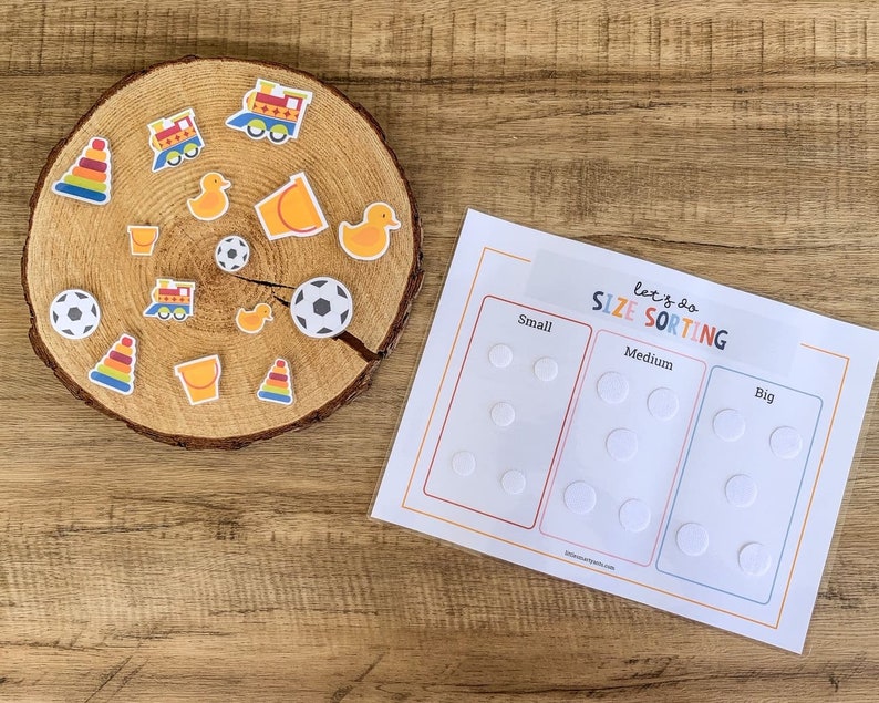 May include: A wooden circle with various colourful toy stickers, including a train, a bucket, a duck, a football, and a stack of rings. A white sheet of paper with the text "Let's do SIZE SORTING" and three columns labelled "Small", "Medium", and "Big" with circles for sorting.
