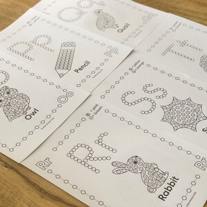Pu&ograve; includere: Un set di fogli di lavoro educativi da colorare bianchi con le lettere dalla O alla T. Ogni pagina mostra una grande lettera formata da cerchi, un'illustrazione corrispondente come un gufo, una matita, una quaglia, un albero, un sole o un coniglio.