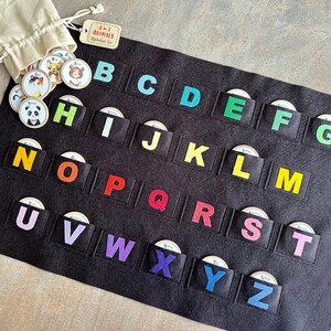 May include: A black felt alphabet board with colorful letters and matching animal picture discs. The board has pockets for each letter, and a drawstring bag holds additional discs. The tag reads "Animals Alphabet Set".