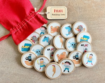 Könnte beinhalten: Ein Piraten-Matching-Spiel mit Holzscheiben mit Piratenfiguren, Schatztruhen und Meeresbewohnern. Das Spiel enthält einen roten Kordelzugbeutel und ein Holzschild mit der Aufschrift "Pirate Matching Game".