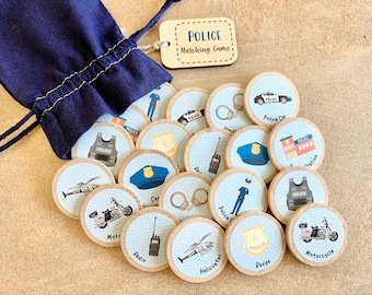 May include: A navy blue drawstring bag with a wooden tag that reads "POLICE Matching Game." Scattered around are wooden discs with police-themed illustrations, including a police car, handcuffs, and a police badge. The game is designed for children.