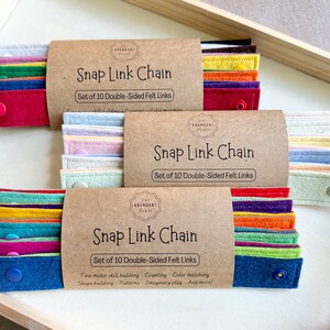 May include: Three sets of Snap Link Chains, each with ten double-sided felt links in various colors. The packaging is brown with the text "Snap Link Chain" and "Set of 10 Double-Sided Felt Links". The felt links are in shades of red, blue, green, yellow, and purple.