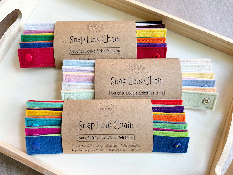 May include: Three sets of Snap Link Chains, each with ten double-sided felt links in various colors. The packaging is brown with the text "Snap Link Chain" and "Set of 10 Double-Sided Felt Links". The felt links are in shades of red, blue, green, yellow, and purple.