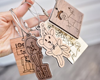Könnte beinhalten: Ein Set aus fünf Holzschlüsselanhängern mit verschiedenen Designs. Jeder Schlüsselanhänger zeigt eine handgezeichnete Illustration auf einer natürlichen Holzoberfläche. Die Schlüsselanhänger sind an silbernen Metallringen befestigt und durch silberne Metallketten verbunden.