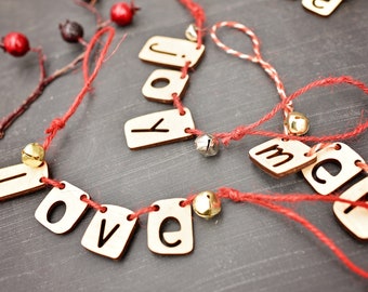 May include: A red and white string garland with wooden letters spelling "I love you" and "Merry" with small gold bells attached.