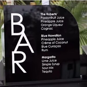 Puede incluir: Señal negra con texto blanco que dice "BAR" y enumera los ingredientes de tres cócteles: The Roberts', Blue Hawaiian y Margarita.