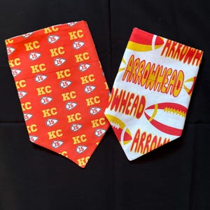 May include: Two red and white dog bandanas. One bandana has a repeating pattern of "KC" and "15" in yellow. The other bandana has the words "Arrowhead" in yellow on a white background.