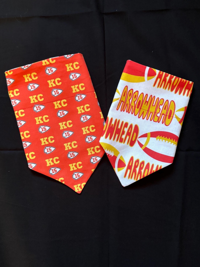 May include: Two red and white dog bandanas. One bandana has a repeating pattern of "KC" and "15" in yellow. The other bandana has the words "Arrowhead" in yellow on a white background.