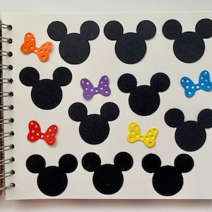 May include: A white page with black Mickey Mouse silhouettes and colourful bow decorations. The page is part of a spiral bound notebook.