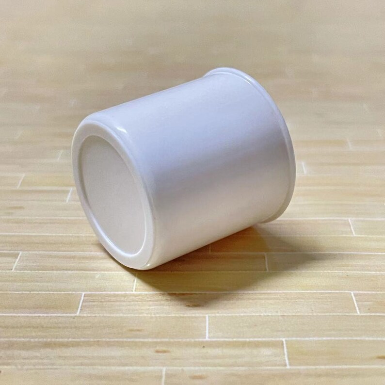 May include: A white plastic cup with a smooth, rounded surface. The cup is lying on its side on a light brown wooden surface.