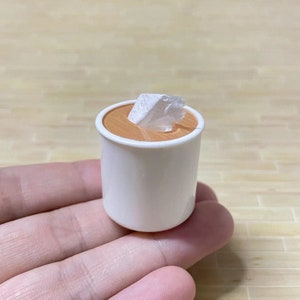 May include: A miniature white ceramic mug with a brown rim, filled with a brown liquid and topped with a white marshmallow.