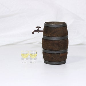 Pode incluir: Um barril de madeira em miniatura com uma torneira de metal e dois pequenos copos cheios de um l&iacute;quido amarelo claro. O barril &eacute; marrom com faixas de metal pretas.