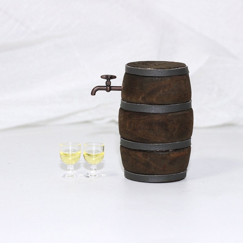 Pode incluir: Um barril de madeira em miniatura com uma torneira de metal e dois pequenos copos cheios de um l&iacute;quido amarelo claro. O barril &eacute; marrom com faixas de metal pretas.