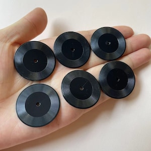 May include: Six black plastic watch face inserts with a circular design and a small hole in the centre.