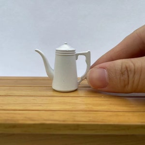 May include: A white ceramic coffee pot with a lid and a handle. The pot is small and is sitting on a wooden surface.