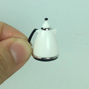 May include: A white miniature electric kettle with a black handle and a black base. The kettle has a silver trim around the top and bottom.